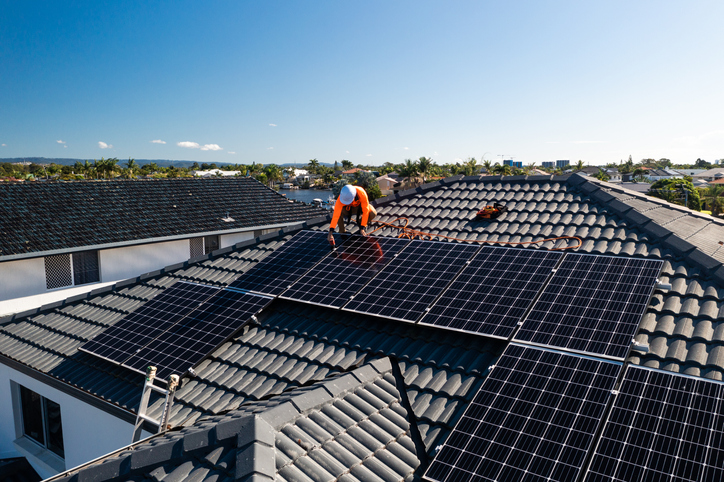 Solar panels and technician on luxury waterfront home on a sunny day.