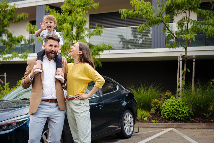 Happy family standing in front their electric car and charging it on the street.