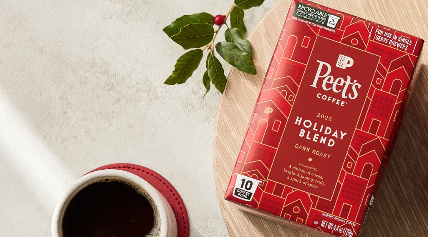 Peet's Coffee Holiday Blend package on a wooden board with a cup of coffee and holly leaves.