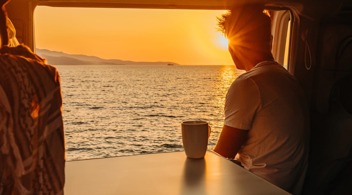 Man in camper looking at a sunrise over the ocean